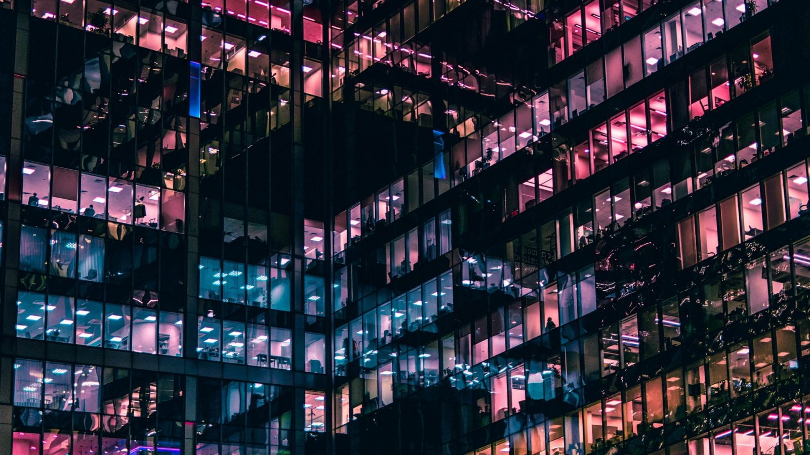 Abstract art showing pink and blue windows of a building at night from a street view. Feature Photo.