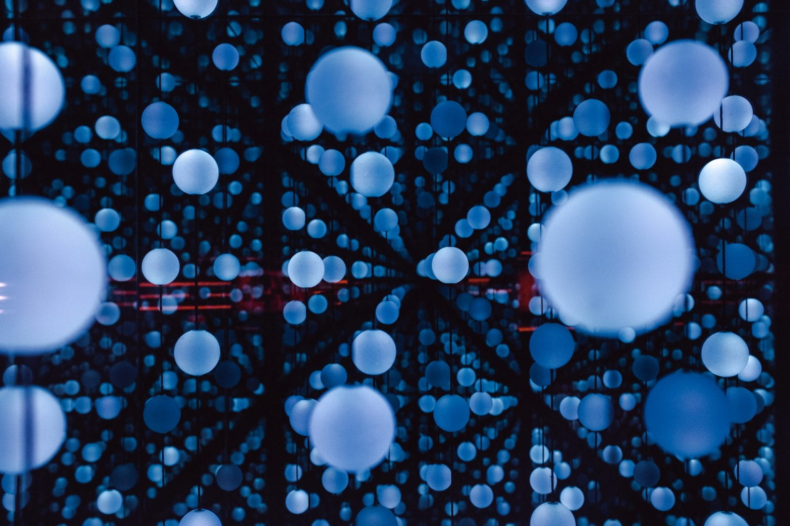 Abstract art of blue spheres on a black backdrop with distant red lines.