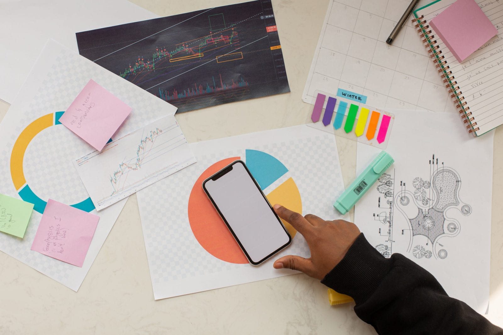 hand touching smart phone on desk, among colorful documents and supplies