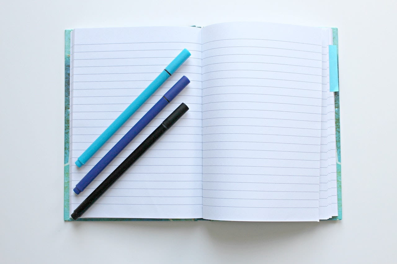 Notebook with three blue pens on it